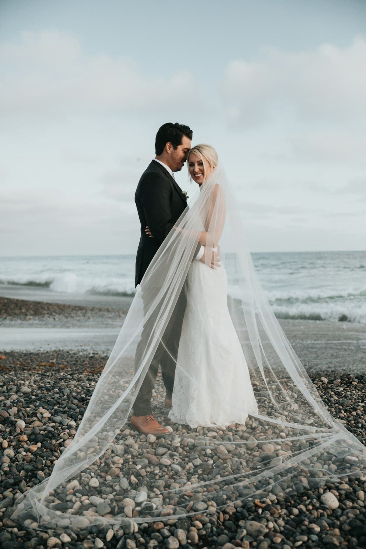 Bride and groom on a pebble beach, veil in the wind