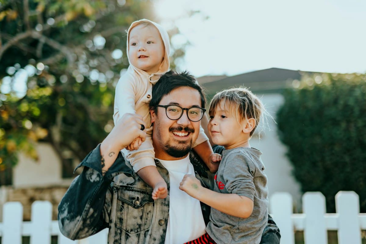 Father with two children on his shoulders by a white fence